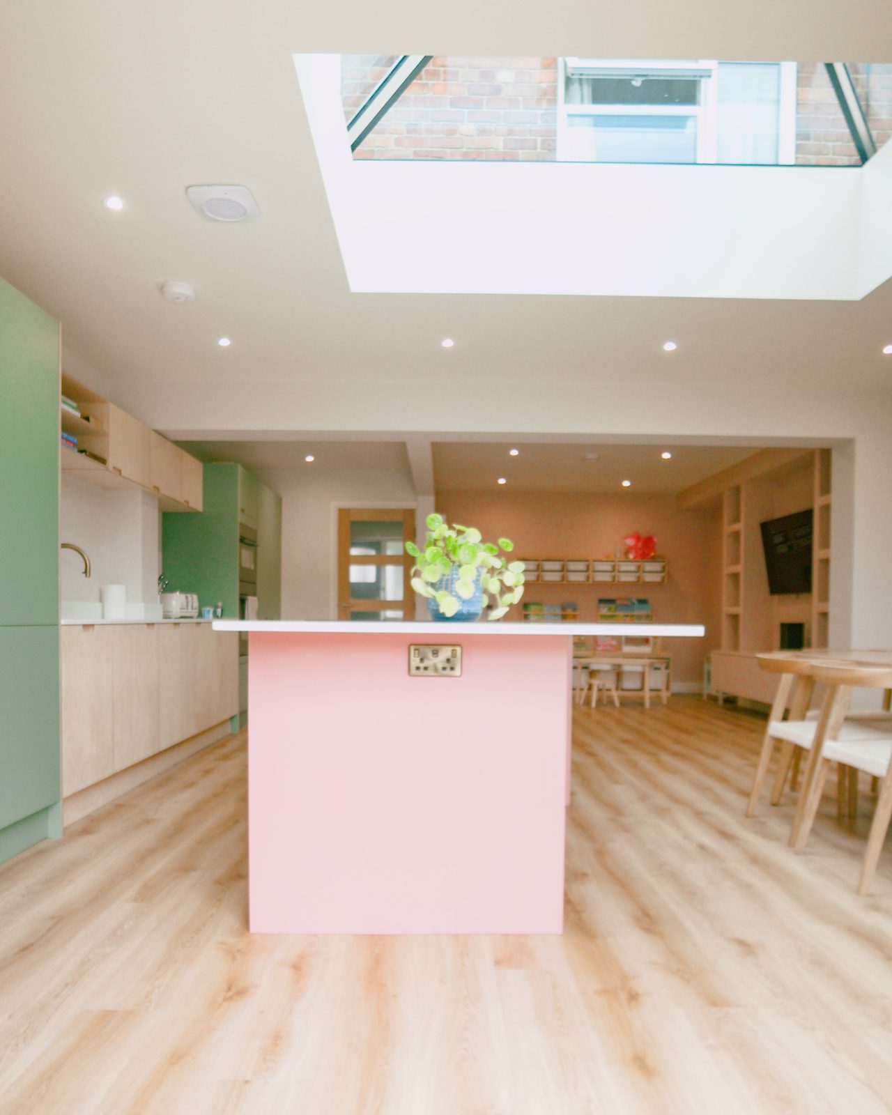 Open-plan kitchen with pink island and roof lantern by JWA Building Services